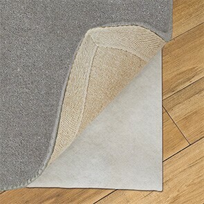 On a solid wood floor a rug underlay is revealed from beneath a grey rug. 
