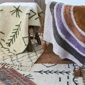 A group of bath mats are hanging from a bathtub and stool, in a variety of prints and patterns.