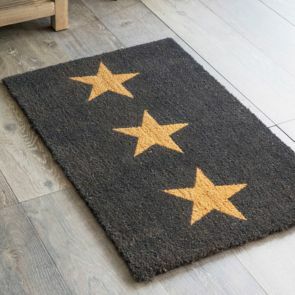 A black door with 3 gold stars in a line is laid on a grey wood effect floor.