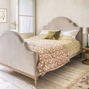 A natural linen, French inspired king size bed with earth toned block printed quilts laid upon the bed in a soft beige bedroom.