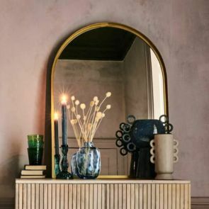 A wood rimmed arched mirror placed on a white-washed cabinet with unique navy vases and candle holders.