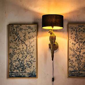 A statue parrot perching on an illuminated wall light framed between two Asian botanical inspired blue wall prints.