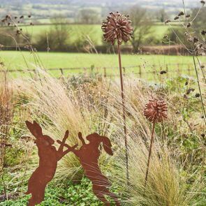 Two rusted iron hares fighting in a overgrown grass meadow framed by the English countryside.