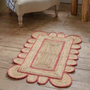 A coral scalloped bordered jute rug is placed on a natural wood floor.