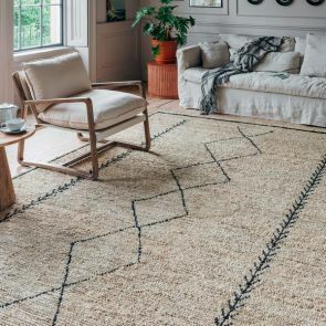 A large cream jute rug sits in the middle of a neutral living room with a minimalist black zig-zag pattern through the centre with two parallel black and white braid on either side.