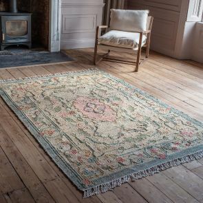 A large kilim rug with a floral tapestry design with a light blue border and a soft pink flower in the center.