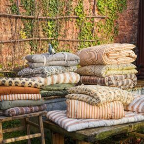 A stack of printed cotton seat pads and seat mats, a cast iron pigeon perches upon them.