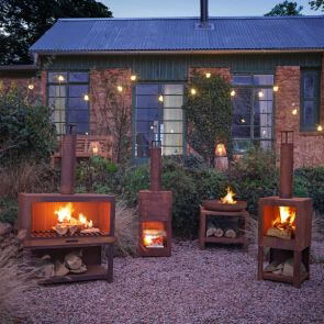 Four lit log burners at dusk in a gravelled garden framed by a string of festoon lights