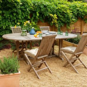Wooden garden dining furniture situated in a tranquil home garden surrounded by shrubbery and plants 