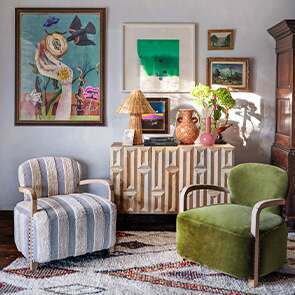 A maximalist living room, filled with two contrasting armchairs, in green and blue and white, decorated with a mix of unique wall prints behind.