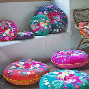 An array of vibrant floral boho seat cushion scattered on the floor and window ledge with a woven in the corner.