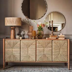 A scandi sideboard with woven door is decorated with golden hues and circular mirrors.