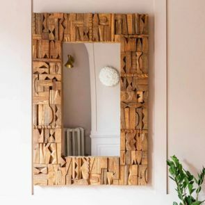 A collaged wooden block framed mirror reflecting a wall light and radiator.