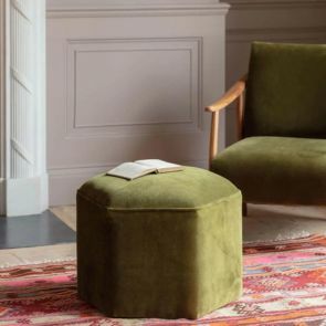 A green hexagonal footstool and matching armchair sit on a contrasting red pattern rug.