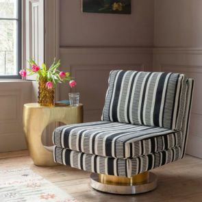 A bold black and white striped pattern swivel chair with a gold base nestled in the corner of a panelled room, a sculptural gold side table sits next to it.